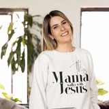 Woman wearing a white sweatshirt with 'This Mama Walks with Jesus' text, holding a laptop in a home setting.